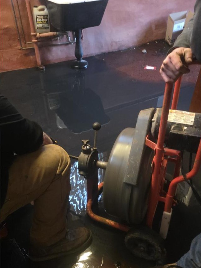 Old School plumber running a drain machine on a backed-up floor drain